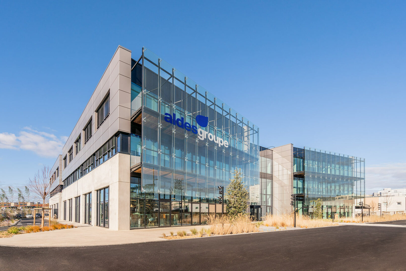 Image d'un grand immeuble de bureaux en verre avec un ciel bleu en arrière-plan. Le bâtiment est le siège social du groupe Aldes, une entreprise française spécialisée dans la ventilation et la climatisation. Le logo Aldes est visible au sommet du bâtiment.