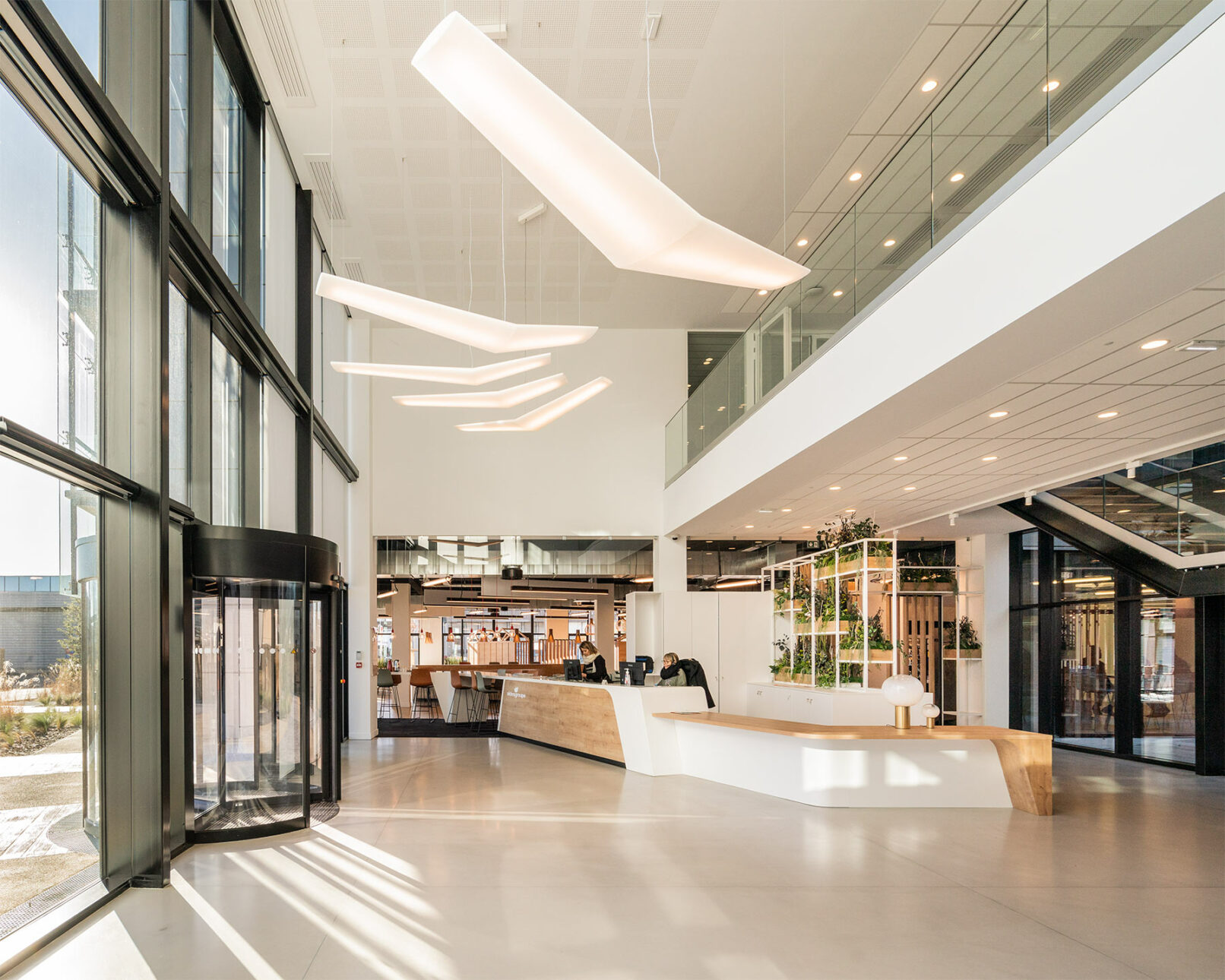 Image du hall d'accueil du siège social d'Aldes, une entreprise française spécialisée dans la ventilation et la climatisation. Le hall est spacieux et lumineux, avec un sol en marbre et des murs blancs. Le comptoir de réception est en bois et est équipé d'un ordinateur et d'un téléphone. Le hall est occupé par deux hôtesses qui parlent entre elles.