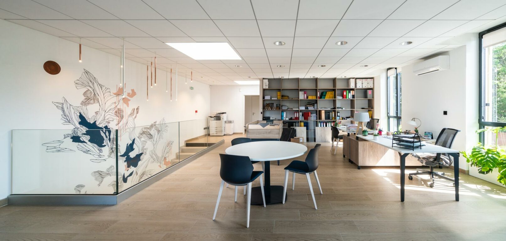 Image de l'open space du siège social de la société Envol à Montpellier, France. L'open space est spacieux et lumineux. Il est décoré de plantes et d'œuvres d'art. Il est équipé de bureaux, de tables de travail et d'un babyfoot